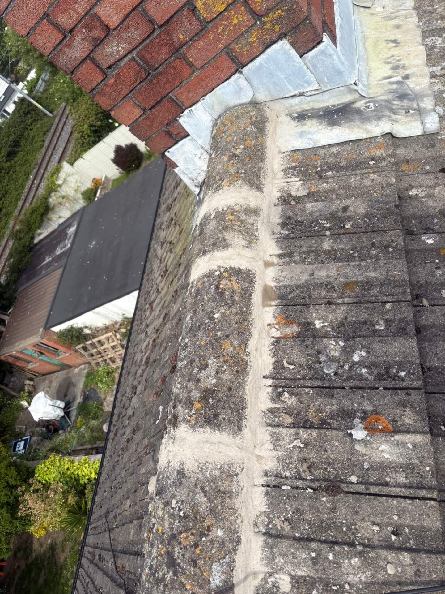 Roof ridge tiles freshly re-bedded and repointed beside a brick chimney