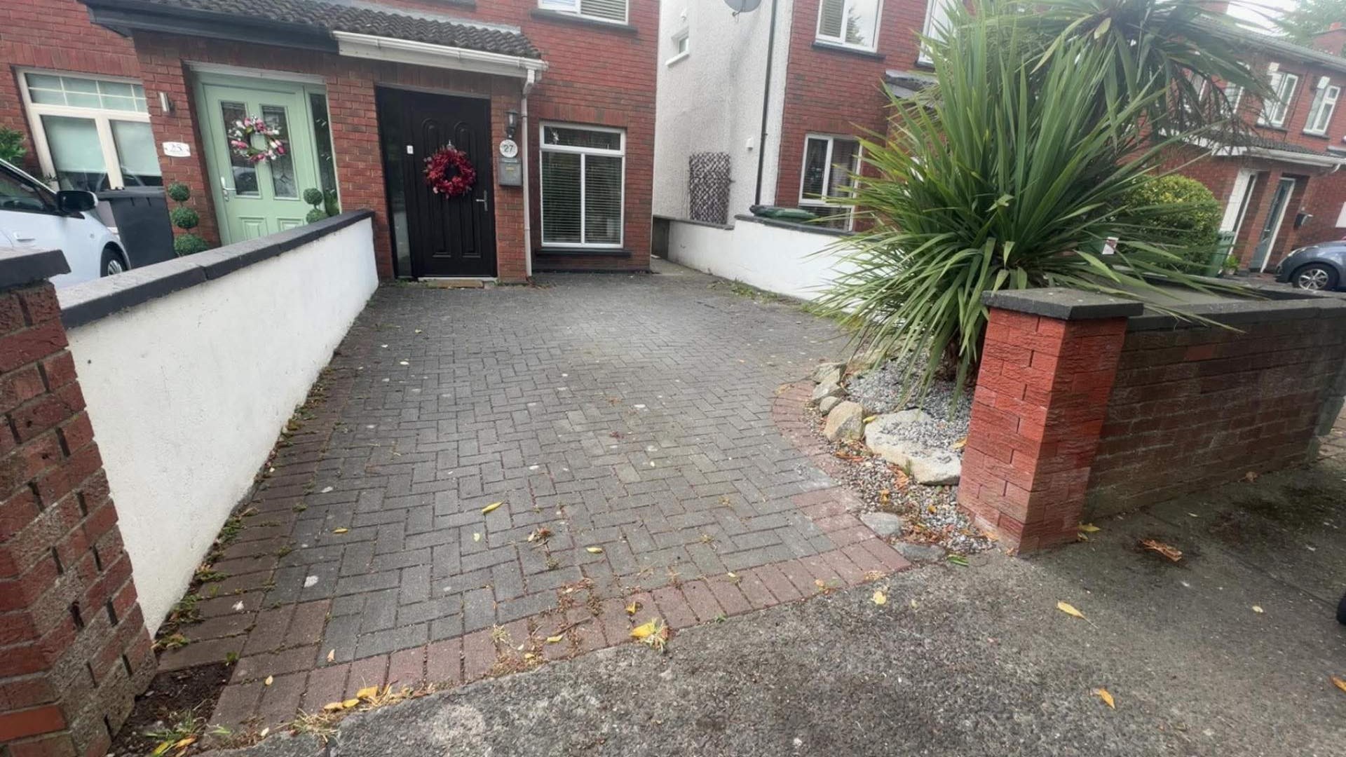 Herringbone brick driveway with weeds and moss through the joints before cleaning