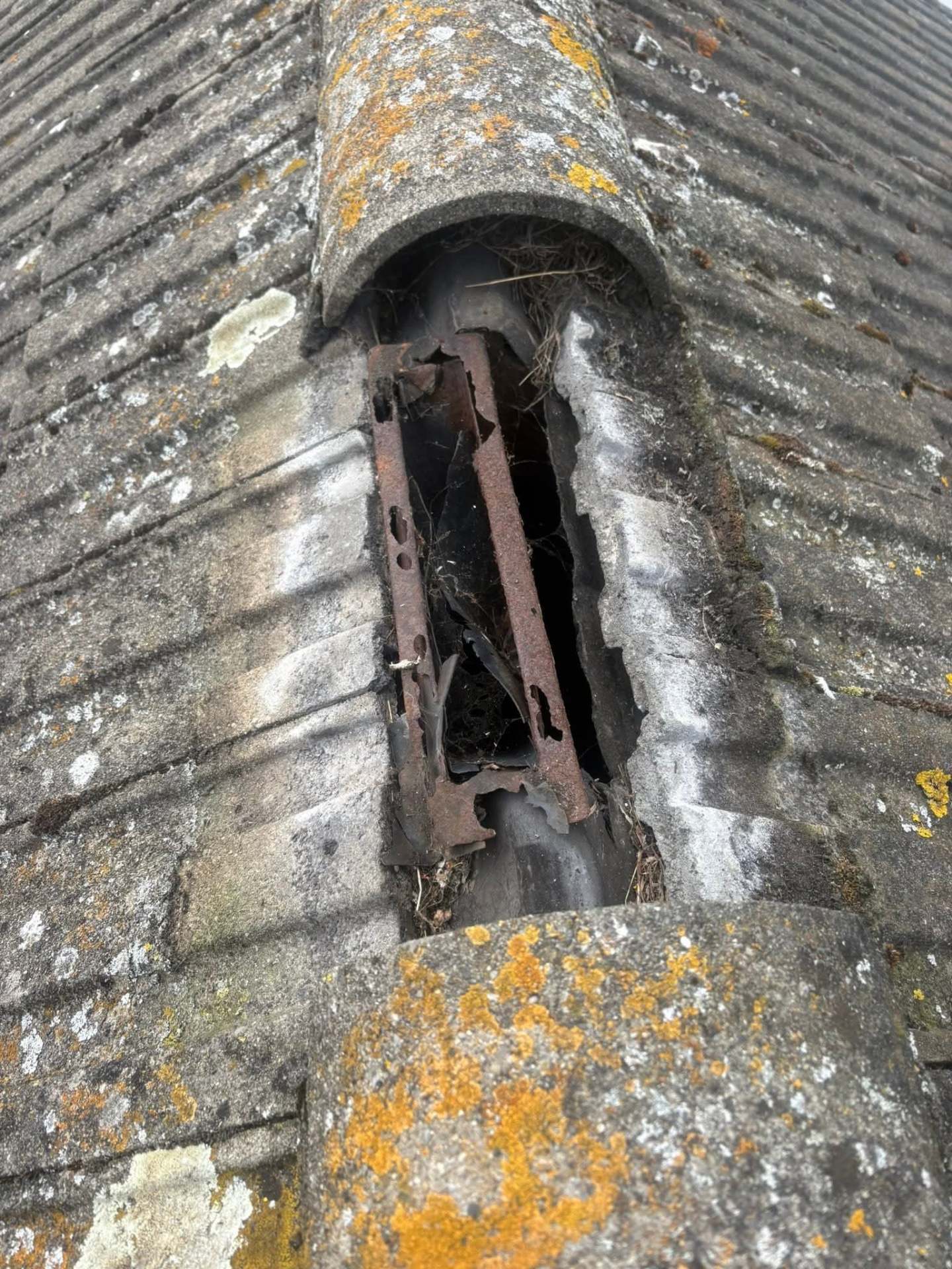 Collapsed ridge section exposing rusted metal and a hole in the roof