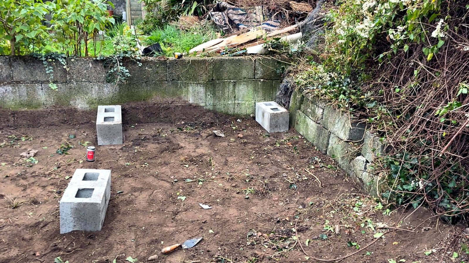 Corner of a garden dug back to bare soil with concrete blocks laid out